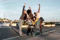 Многорасовая группа молодых женщин, стоящих вокруг тележки с покупками на дороге — стоковое фото