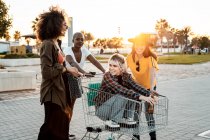 Многорасовая группа молодых женщин, стоящих вокруг тележки с покупками на дороге — стоковое фото