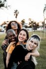 Multiethnische Gruppe junger lachender Freundinnen in lässiger Kleidung, die Spaß haben und miteinander auf dem Rasen kuscheln — Stockfoto