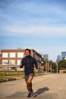 Concentrated Hispanic male athlete in sportswear with headphones running along empty road at downtown of Dallas, Texas — Stock Photo