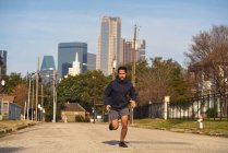 Сконцентрированный латиноамериканец в спортивной одежде с наушниками, бегущими по пустой дороге в центре Далласа, штат Техас — стоковое фото