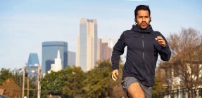 Concentrated Hispanic male athlete in sportswear with headphones looking away as running along empty road at downtown — Stock Photo