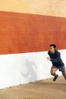 Vue latérale de fit homme sportif hispanique écouter de la musique tout en faisant du jogging le long de la rue de la ville à Dallas — Photo de stock