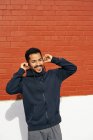 Hombre hispano con ropa casual sonriendo y mirando hacia otro lado mientras disfruta de la música usando auriculares en la calle de la ciudad en Dallas, Texas - foto de stock