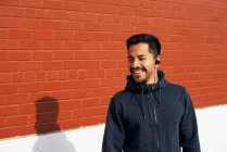 Zufriedener hispanischer Mann in Freizeitkleidung, der lächelt und wegschaut, während er in der City Street in Dallas, Texas Musik über Kopfhörer genießt — Stockfoto