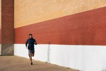 Вид сбоку спортивного мужчины в спортивном костюме, который активно слушает музыку во время пробежки по городской улице в Далласе — стоковое фото