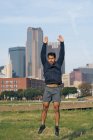 Atleta masculino hispano en activo saltando con los brazos extendidos con el centro de Dallas, Texas, EE.UU. - foto de stock