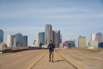 Hispanische Joggerin in lässigem Kapuzenpulli mit Kopfhörern beim Laufen mit blauem Himmel über der Innenstadt von Dallas, Texas — Stockfoto