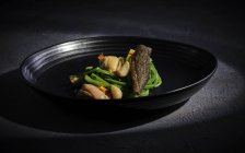 Exquisites Fleisch mit Knoblauchgemüse auf breitem schwarzen Teller serviert — Stockfoto