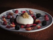 Noce grattugiata su dessert cremoso con marmellata circondata da pezzi di fragole, mirtilli e lamponi su piatto bianco — Foto stock