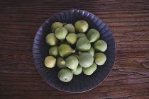 From above of blue ornamental bowl full of soft fresh figs on dark wooden table — Stock Photo