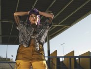 From below stylish woman with purple hairstyle in yellow pants standing in street and looking in camera — Stock Photo