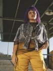 From below stylish woman with purple hairstyle in yellow pants standing in street and looking in camera — Stock Photo