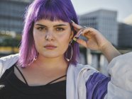 Modefrau mit lila Frisur berührt Gesicht und blickt selbstbewusst in die Kamera — Stockfoto