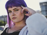 Крупним планом жінка з фіолетовою зачіскою торкається обличчя в центрі міста і впевнено дивиться в камеру — стокове фото