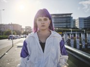 Stylish woman with purple hairstyle in trendy wear posing in urban bridge in city — Stock Photo