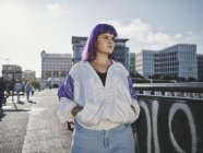 Stylische Frau mit lila Frisur in trendiger Kleidung posiert auf der städtischen Brücke in der Stadt — Stockfoto