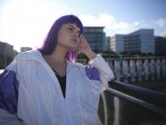 Mujer elegante con peinado púrpura en ropa de moda posando en puente urbano en la ciudad - foto de stock