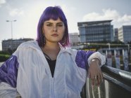 Stylische Frau mit lila Frisur in trendiger Kleidung posiert auf der städtischen Brücke in der Stadt — Stockfoto