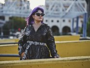 Модная уверенная в себе женщина с фиолетовой прической в блестящем черном пиджаке в ярком дневном городе — стоковое фото