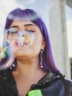 Porträt einer modischen Frau mit lila Haaren, die mit gepflegter Hand Blasen weht — Stockfoto