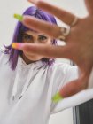 Femme souriante de mode avec des cheveux violets geste avec la main soignée avec des anneaux sur les doigts, regardant à la caméra — Photo de stock