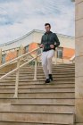 From below of focused male in casual wear with earphones with phone in hand training legs jogging down on stairs in urban street — Stock Photo