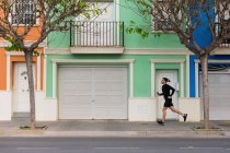 Вид сбоку активного парня в наушниках с телефоном в руках, бегущего по городской улице — стоковое фото