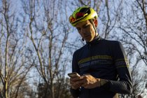 Велосипедист отдыхает, пользуясь мобильным телефоном на велосипедной дорожке в парке — стоковое фото