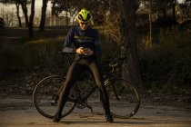 Homme cycliste se reposant tout en utilisant un téléphone portable sur la piste cyclable dans un parc — Photo de stock