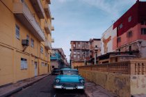 Small street with vintage car in roadside between historical colorful buildings with bars on windows in Cuba — Stock Photo