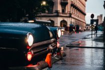 Cappuccio di auto d'epoca blu con luci accese e vecchia auto rossa in movimento sullo sfondo sul tempo piovoso a Cuba — Foto stock