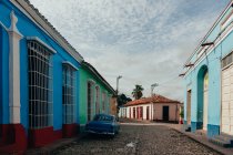 Небольшая улица с булыжником и старинный автомобиль в придорожной между историческими красочными зданиями с решетками на окнах на Кубе — стоковое фото