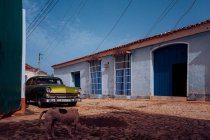 Небольшая улица с винтажным автомобилем на обочине между историческими красочными зданиями с решетками на окнах на Кубе — стоковое фото