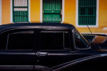 Kleine Straße mit schwarzem Oldtimer am Straßenrand zwischen historischen, bunten Gebäuden mit Gittern an den Fenstern in Kuba — Stockfoto