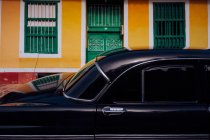Small street with black vintage car in roadside between historical colorful buildings with bars on windows in Cuba — Stock Photo