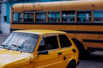 Retro yellow vintage car and yellow school bus on city street with old buildings — Stock Photo