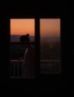 Боковой вид молодой безликой женщины, стоящей на балконе с великолепным закатом на размытом фоне — стоковое фото