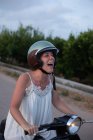 Весела жінка у відпустці в легкому одязі посміхається з закритими очима на мотоциклі в русі по дорозі — стокове фото