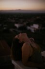 Peaceful woman leaning with closed eyes on fence of balcony with sunset on blurred background — Stock Photo