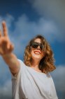 From below stylish brown curly haired woman with red lipstick in trendy sunglasses looking at camera with blue sky on the background — Stock Photo