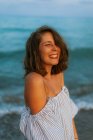 Donna felice in abito leggero a piedi tra le piccole onde del mare sulla costa vuota al tramonto con gli occhi chiusi — Foto stock