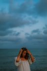 Donna in abito leggero che cammina tra piccole onde marine sulla costa vuota al crepuscolo guardando in basso — Foto stock