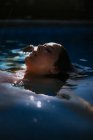 Vista laterale del viso sopra la superficie dell'acqua di riposo donna tranquilla con gli occhi chiusi in piscina nella soleggiata giornata estiva — Foto stock