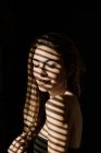 Stripe shadow from shutters falling on face of charming relaxed long haired woman smiling with closed eyes — Stock Photo