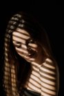 Sombra de listra de persianas que caem na cara da mulher de cabelos longos relaxada encantadora que sorri com olhos fechados — Fotografia de Stock