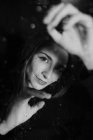 Черное и белое от улыбающейся женщины, стоящей за стеклом в каплях воды касаясь поверхности и глядя на камеру — стоковое фото