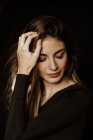 Sensual mulher linda em vestido escuro tocando cabelos longos e brilhantes e pensando com os olhos fechados — Fotografia de Stock