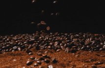 Падение свежие жареные кофейные зерна и порошковый кофе изолированы на черном фоне — стоковое фото