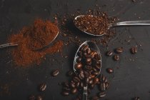 Types of coffee grounds instant and powder and coffee beans in spoons on black table — Stock Photo